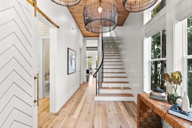 stairs with a towering ceiling, a chandelier, wooden ceiling, and hardwood / wood-style floors