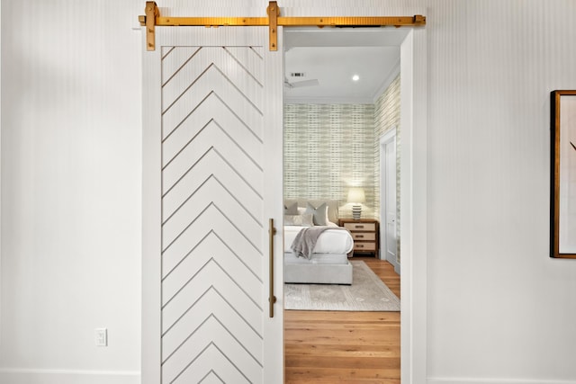 bedroom featuring ornamental molding, hardwood / wood-style floors, and a barn door