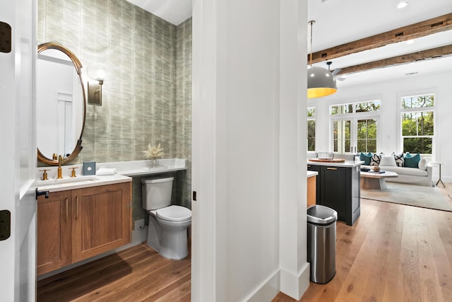 bathroom featuring toilet, vanity, hardwood / wood-style floors, and beamed ceiling