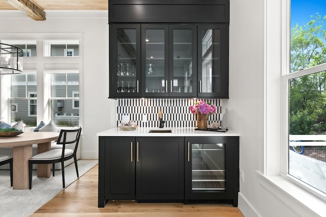 bar featuring light wood-type flooring, beam ceiling, wine cooler, and sink