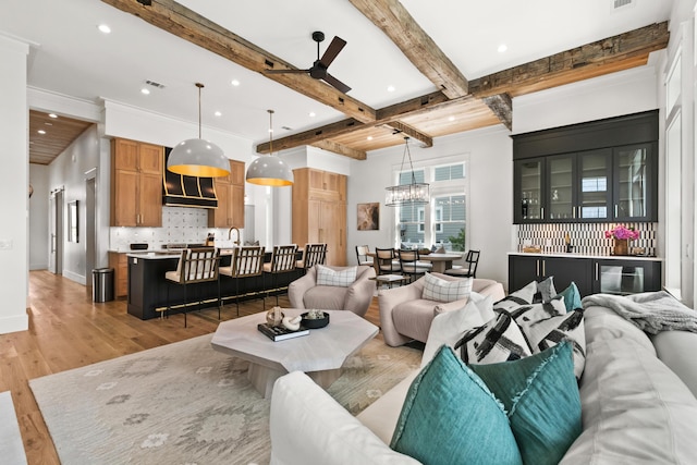 living room with light hardwood / wood-style floors, beamed ceiling, ceiling fan with notable chandelier, coffered ceiling, and sink