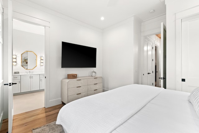 bedroom with sink, ensuite bathroom, light wood-type flooring, and ornamental molding