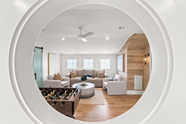 living room with ceiling fan, light wood-type flooring, vaulted ceiling, and a barn door