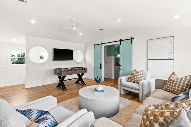 living room with light hardwood / wood-style floors, ceiling fan, vaulted ceiling, and a barn door