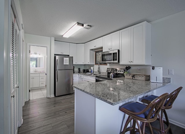 kitchen with a kitchen breakfast bar, stainless steel appliances, kitchen peninsula, a textured ceiling, and white cabinetry