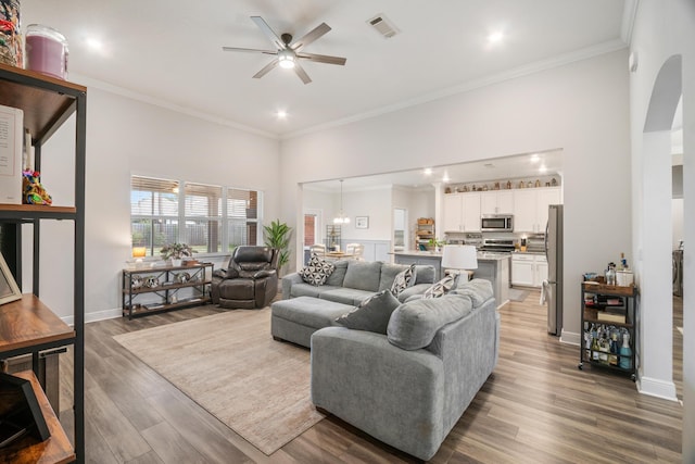 living room with hardwood / wood-style flooring, ornamental molding, and ceiling fan with notable chandelier