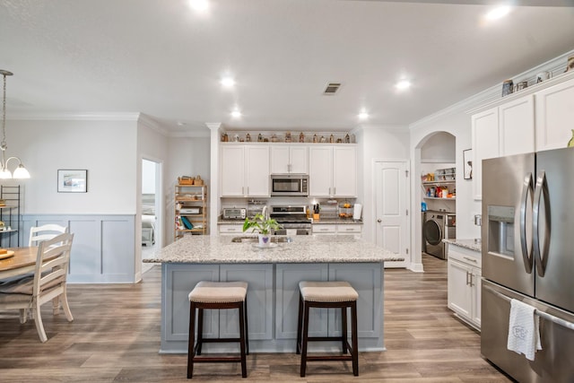 kitchen with decorative light fixtures, white cabinets, appliances with stainless steel finishes, and an island with sink