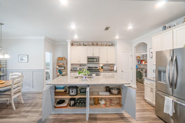 kitchen with an island with sink, washer / dryer, stainless steel appliances, and pendant lighting