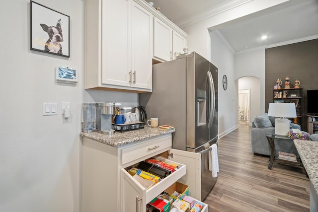 kitchen with white cabinetry, light hardwood / wood-style flooring, stainless steel fridge with ice dispenser, ornamental molding, and light stone counters