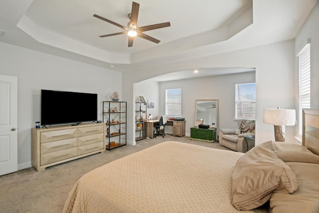 bedroom with ceiling fan, carpet flooring, a raised ceiling, and multiple windows