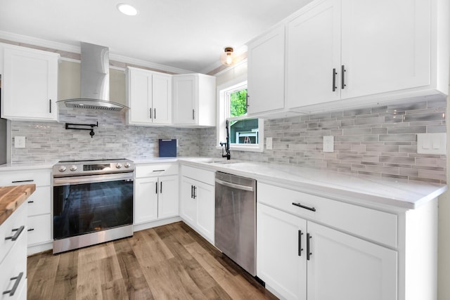 kitchen with stainless steel appliances, wall chimney range hood, white cabinets, and decorative backsplash