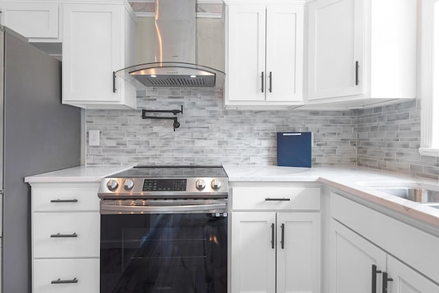 kitchen with white cabinets, stainless steel electric stove, wall chimney range hood, and tasteful backsplash