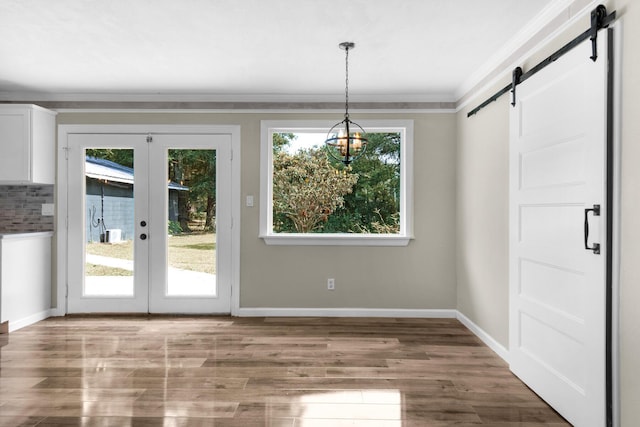 unfurnished dining area with a barn door, french doors, hardwood / wood-style floors, and crown molding