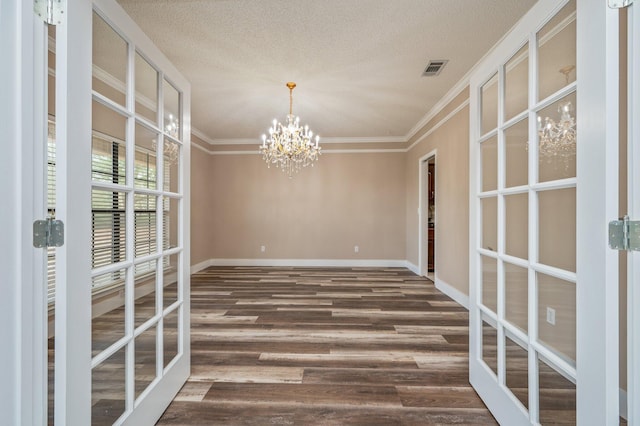 empty room with french doors, an inviting chandelier, ornamental molding, a textured ceiling, and dark hardwood / wood-style floors