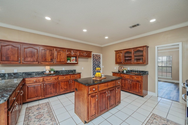 kitchen with light tile patterned floors, crown molding, dark stone countertops, and a center island