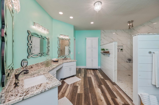 bathroom with a textured ceiling, hardwood / wood-style flooring, vanity, and tiled shower