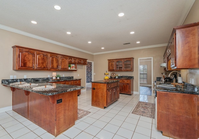 kitchen with dark stone countertops, a kitchen island, light tile patterned flooring, ornamental molding, and kitchen peninsula