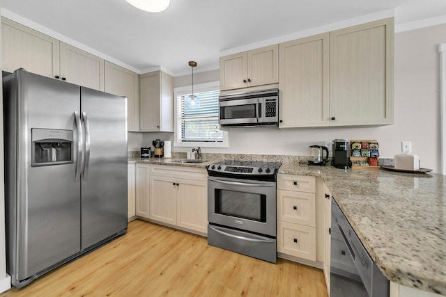 kitchen with sink, pendant lighting, stainless steel appliances, light stone countertops, and light hardwood / wood-style floors