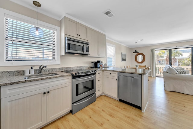 kitchen with sink, appliances with stainless steel finishes, kitchen peninsula, pendant lighting, and light hardwood / wood-style floors