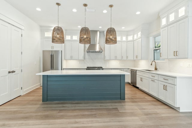 kitchen featuring appliances with stainless steel finishes, wall chimney exhaust hood, sink, and white cabinets