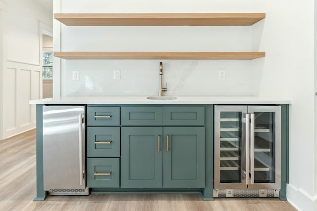 bar featuring sink, stainless steel fridge, green cabinetry, beverage cooler, and light wood-type flooring