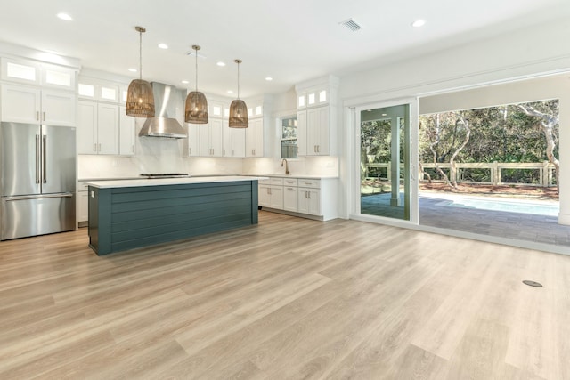 kitchen featuring wall chimney exhaust hood, white cabinetry, decorative light fixtures, appliances with stainless steel finishes, and backsplash