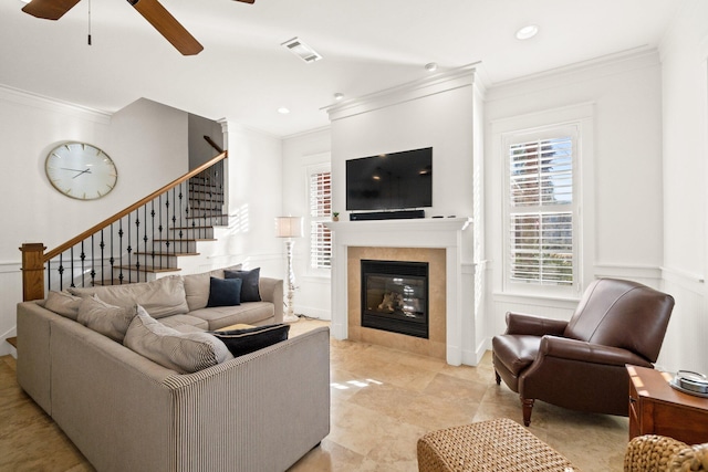 living room with ceiling fan, a tile fireplace, and ornamental molding