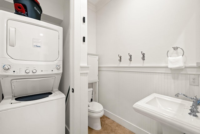 clothes washing area with stacked washing maching and dryer, wooden walls, and sink