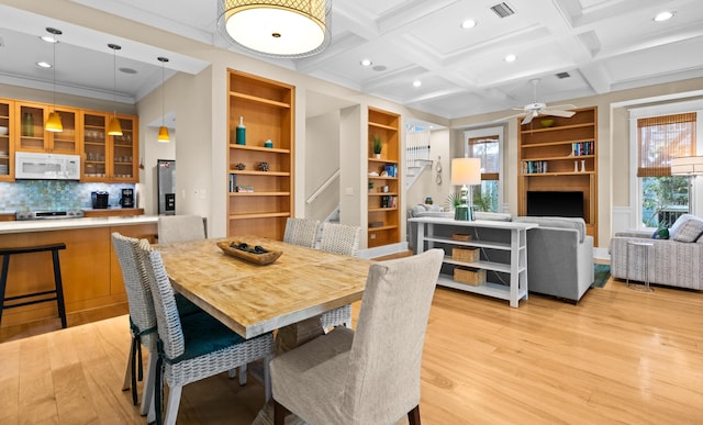 dining space featuring ceiling fan, built in shelves, coffered ceiling, and light hardwood / wood-style floors