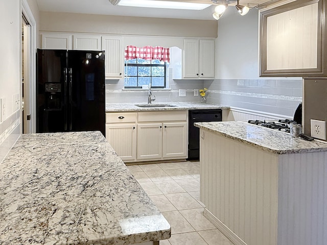 kitchen with light stone countertops, white cabinets, black appliances, sink, and light tile patterned floors