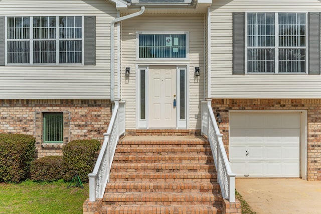 entrance to property featuring a garage, concrete driveway, and brick siding