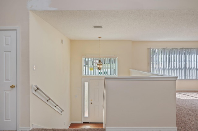 entryway featuring carpet floors, visible vents, a textured ceiling, a chandelier, and baseboards