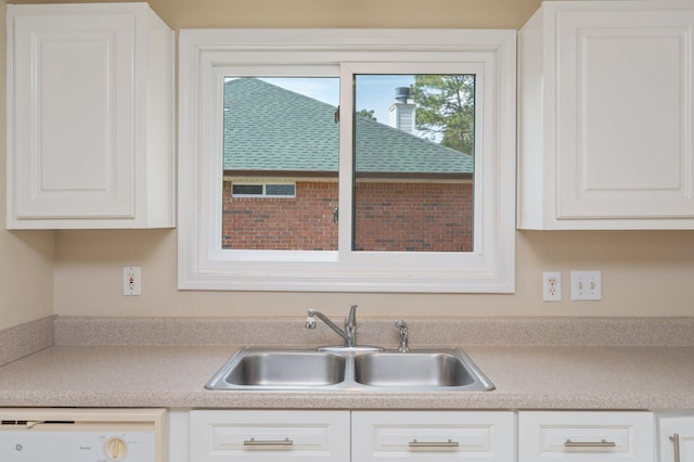 kitchen featuring dishwasher, light countertops, a sink, and white cabinetry