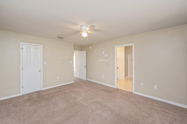 unfurnished bedroom featuring a textured ceiling, carpet floors, visible vents, baseboards, and ensuite bath