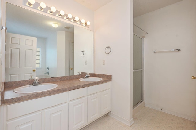 bathroom with double vanity, an enclosed shower, a sink, and baseboards