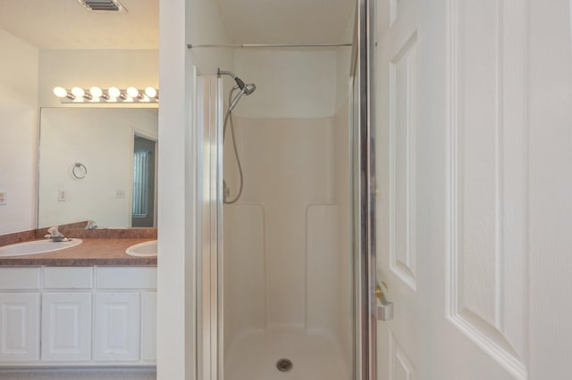 bathroom featuring double vanity, a shower stall, visible vents, and a sink