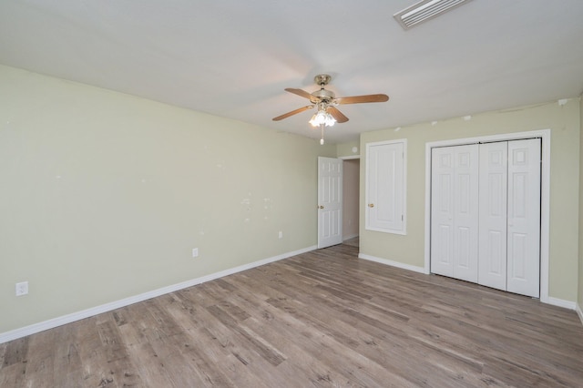 unfurnished bedroom featuring a closet, visible vents, a ceiling fan, wood finished floors, and baseboards