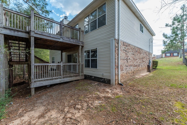 back of house featuring brick siding, a lawn, and a deck