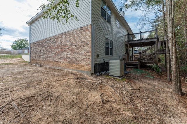 view of property exterior with cooling unit, brick siding, a wooden deck, and stairs