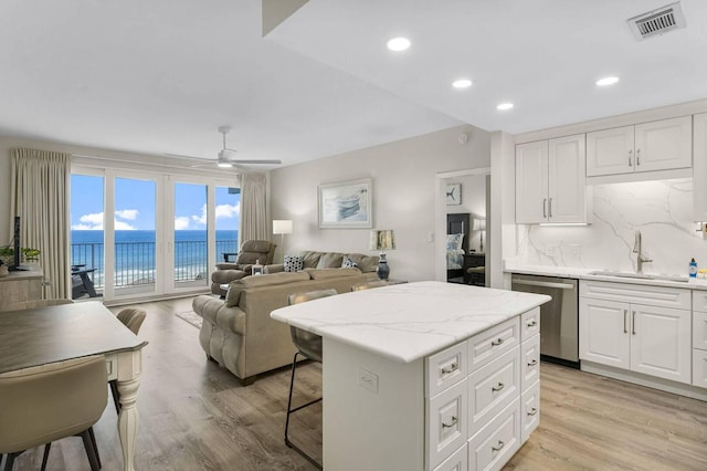 kitchen with a center island, a water view, sink, white cabinetry, and stainless steel dishwasher