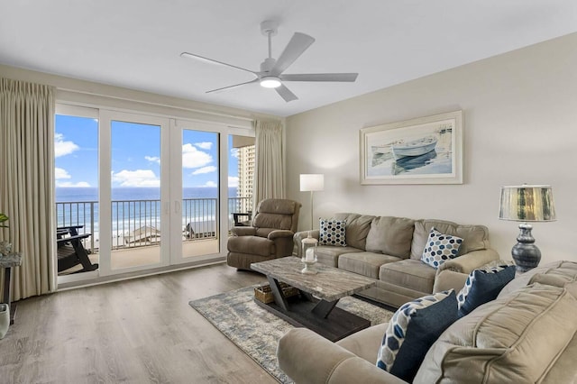 living room with ceiling fan, a water view, a beach view, and wood-type flooring