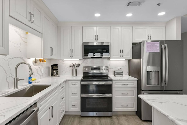 kitchen featuring appliances with stainless steel finishes, white cabinets, light stone countertops, and sink