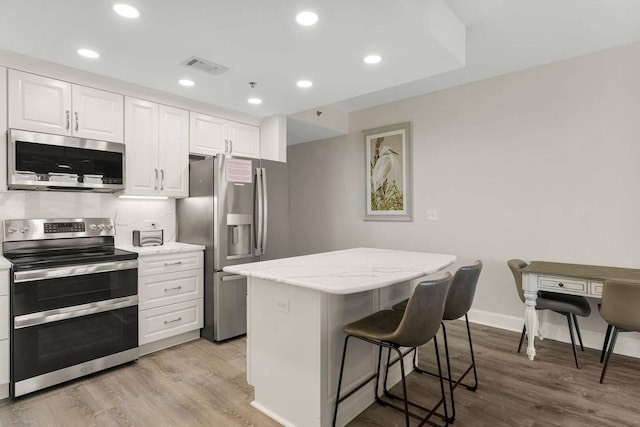 kitchen featuring stainless steel appliances, a center island, white cabinetry, light hardwood / wood-style floors, and light stone countertops