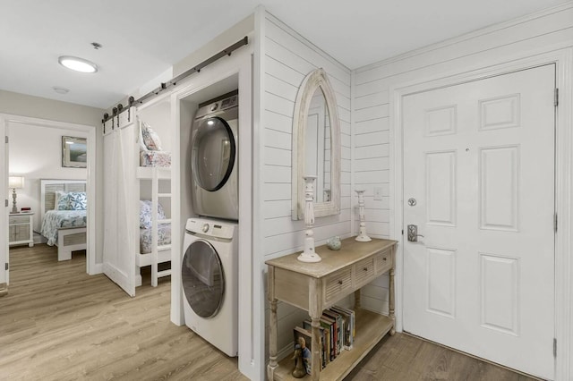 laundry area with stacked washer and clothes dryer, wooden walls, a barn door, and light hardwood / wood-style flooring