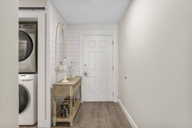 washroom featuring wood-type flooring, wooden walls, and stacked washer / dryer