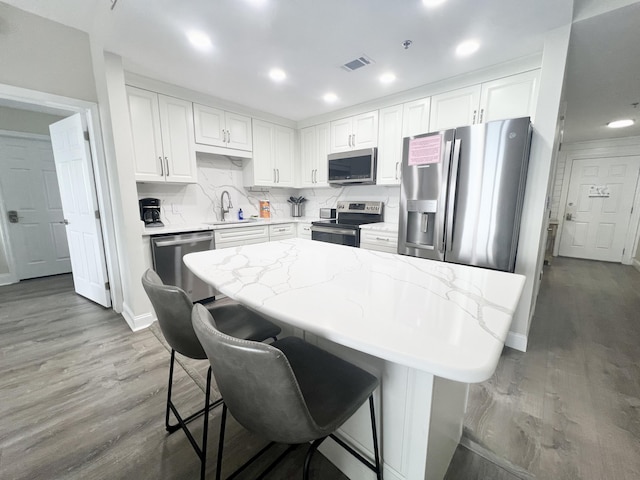 kitchen with light hardwood / wood-style flooring, a breakfast bar area, appliances with stainless steel finishes, white cabinetry, and sink