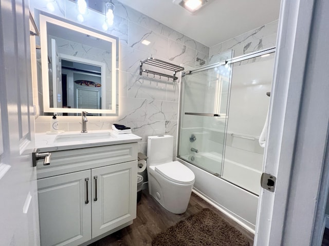 full bathroom with tile walls, combined bath / shower with glass door, hardwood / wood-style flooring, toilet, and vanity