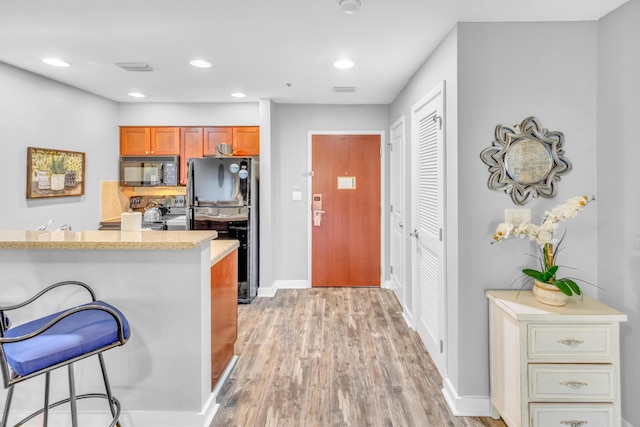 kitchen featuring black appliances, a breakfast bar, light wood-type flooring, and kitchen peninsula