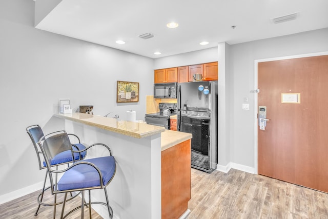 kitchen with a kitchen breakfast bar, light hardwood / wood-style flooring, kitchen peninsula, and black appliances