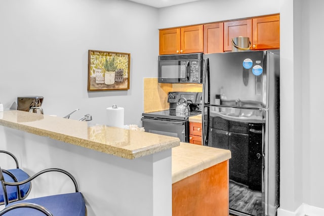 kitchen featuring decorative backsplash, black appliances, kitchen peninsula, and a breakfast bar area